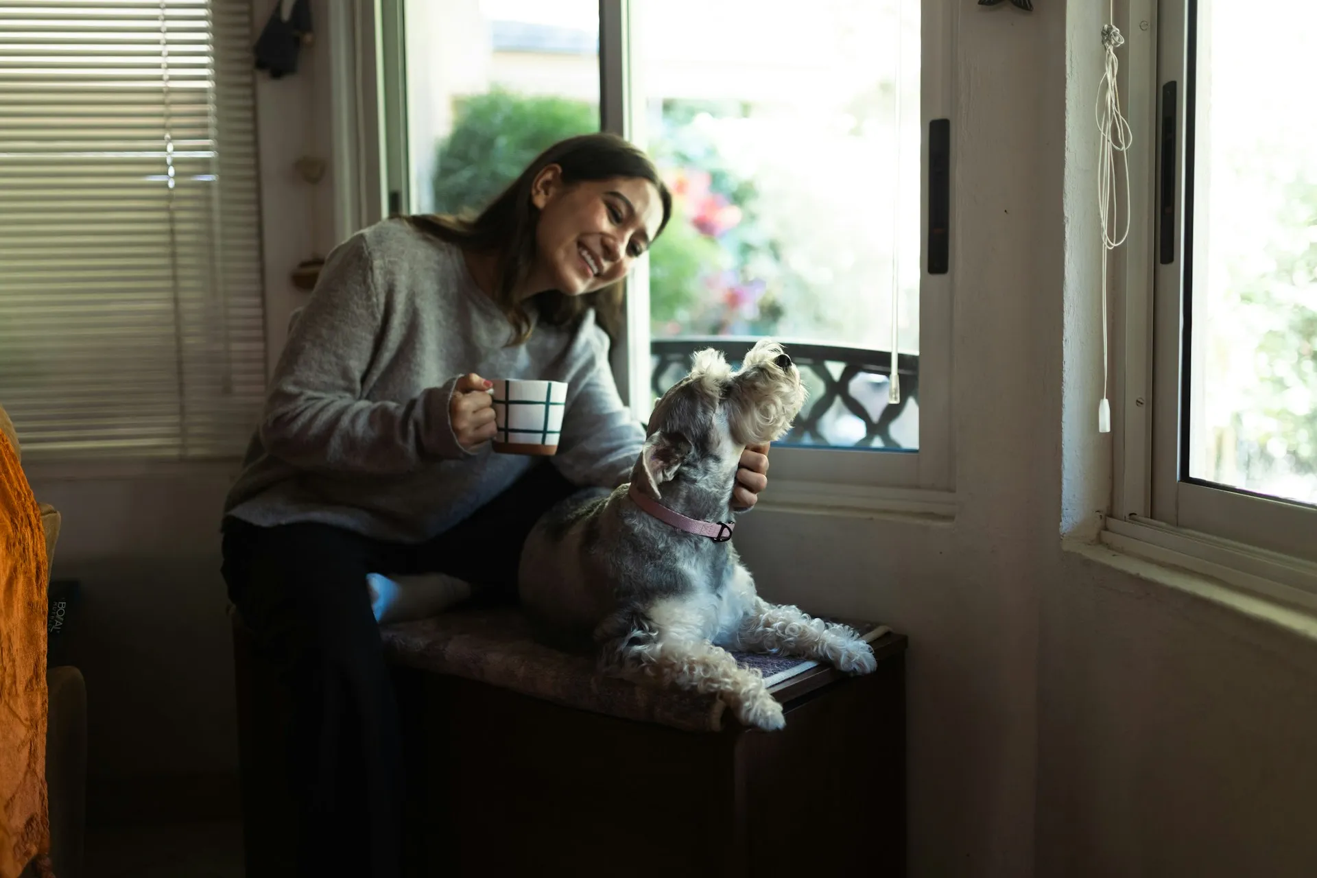 A woman holding a coffee mug with a dog sits on a bench beside her.